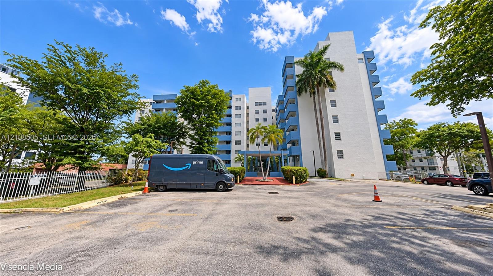 Multi-story mid-rise exterior featuring white masonry facade, blue structural accents, and mature palm landscaping