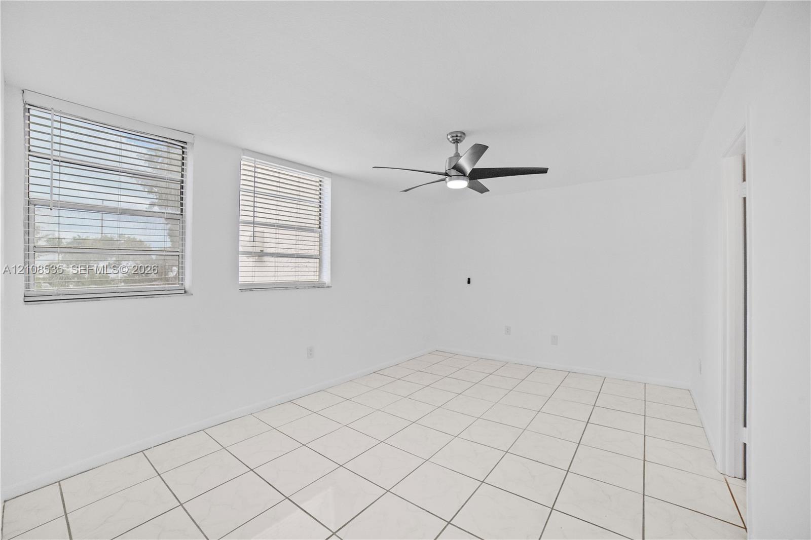 Interior space featuring white tile flooring, neutral walls, two horizontal-slat windows, and a brushed-nickel ceiling fan with integrated lighting