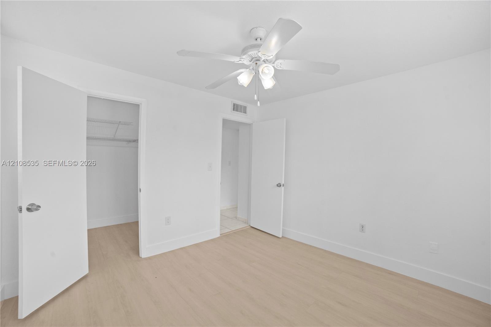 Room featuring wood-finish flooring, a white ceiling fan with integrated lighting, and built-in closet shelving