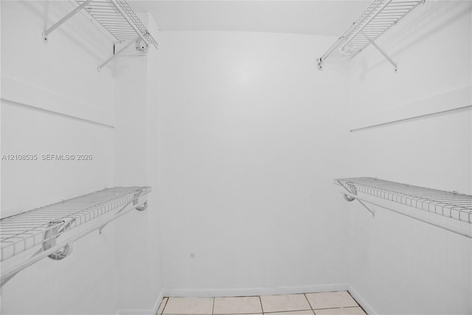 Storage space featuring white walls, tile flooring, and dual-level wire shelving
