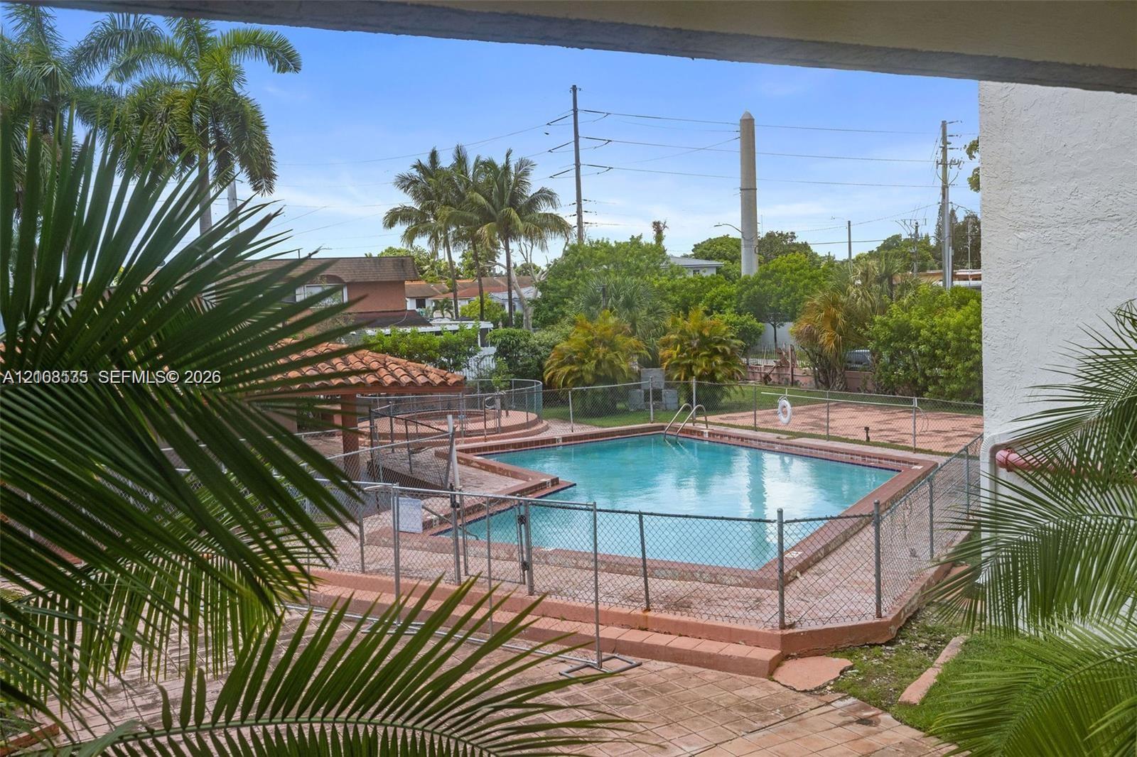 Outdoor swimming pool with tile decking, surrounding metal fencing, and mature palm trees