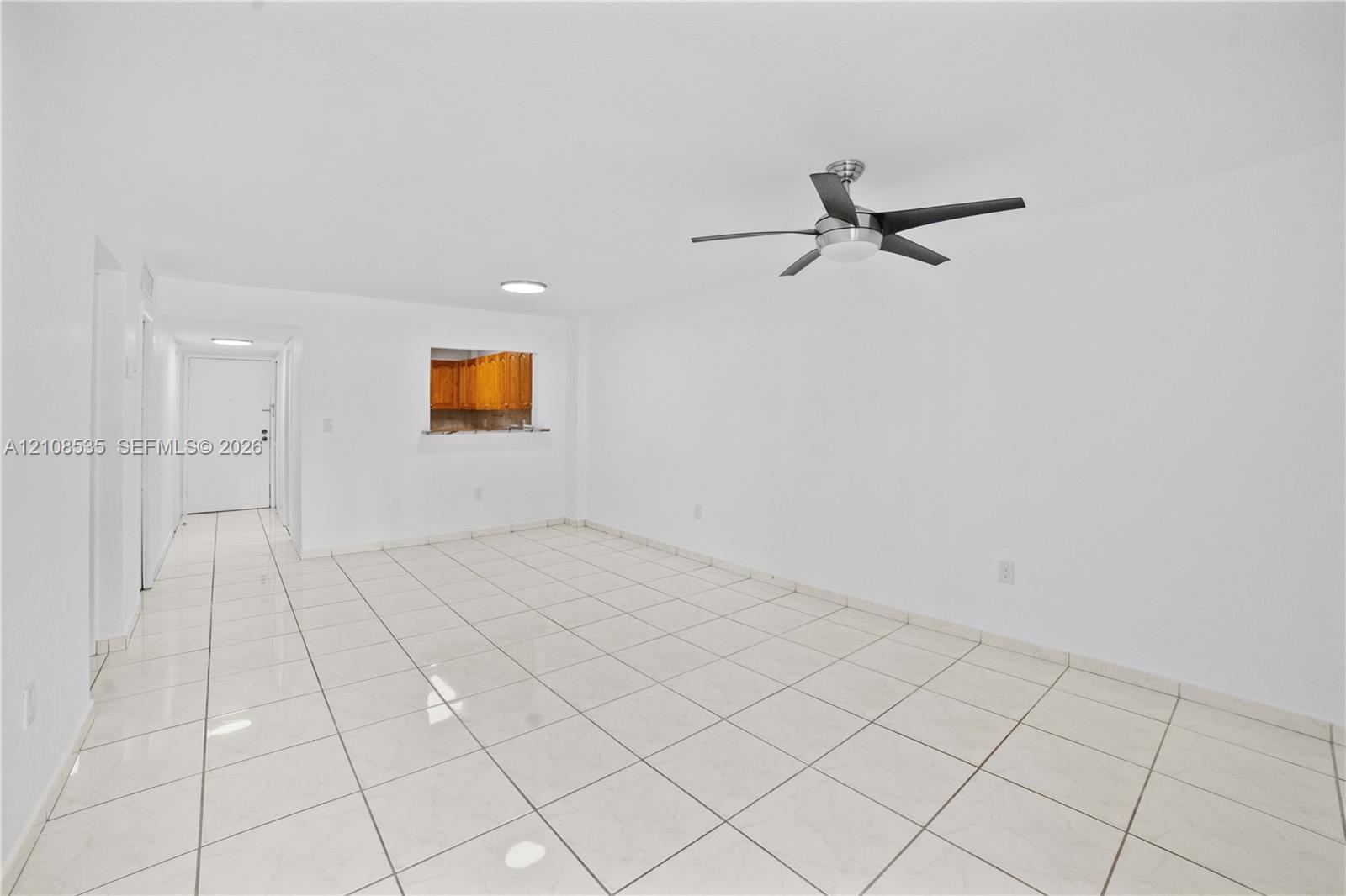 Interior space featuring neutral white walls, ceramic tile flooring, a brushed metal ceiling fan with integrated lighting, and a pass-through opening