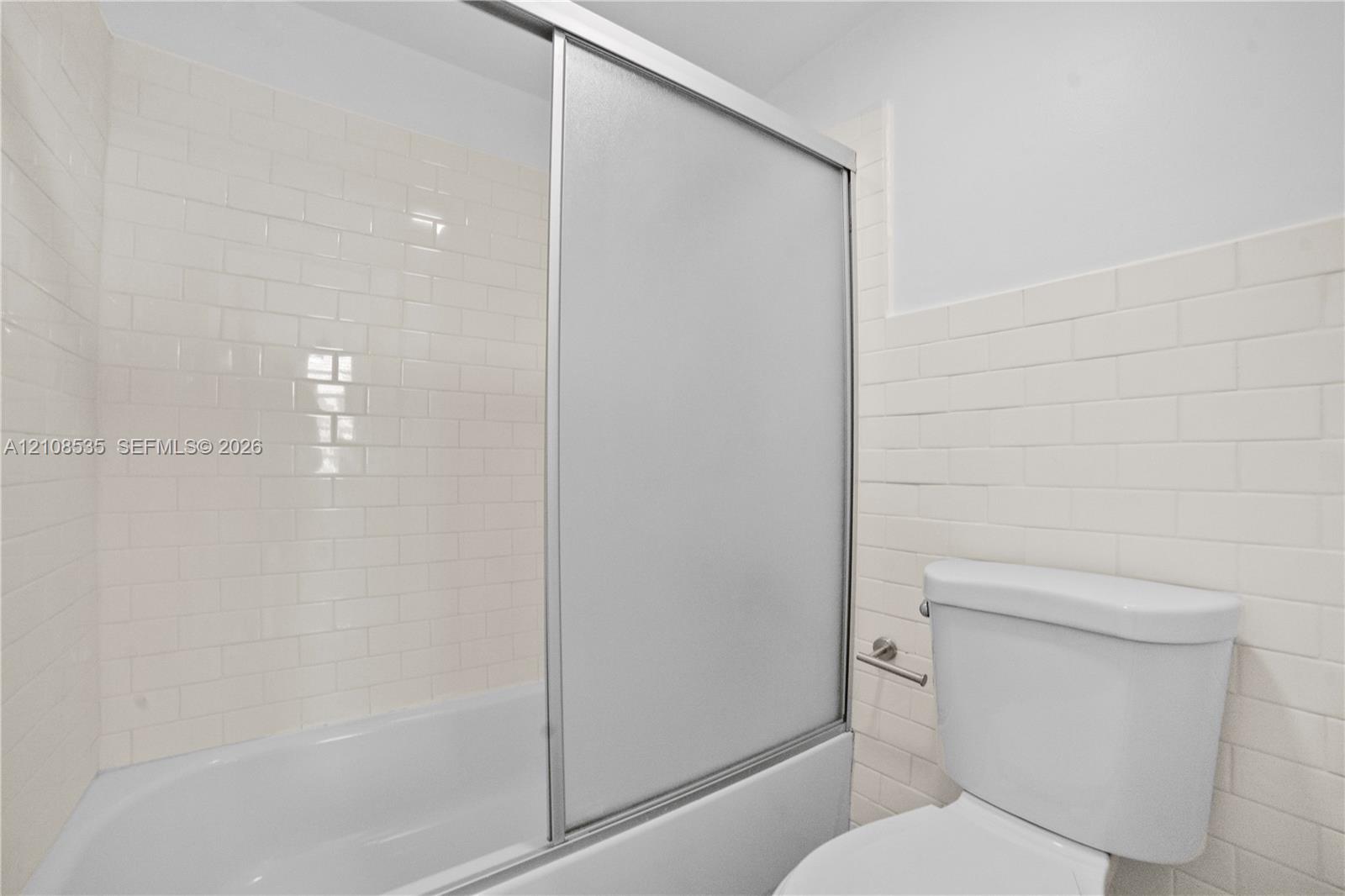 Full-height white subway tile surround, integrated bathtub, frosted glass sliding shower enclosure, and standard porcelain toilet
