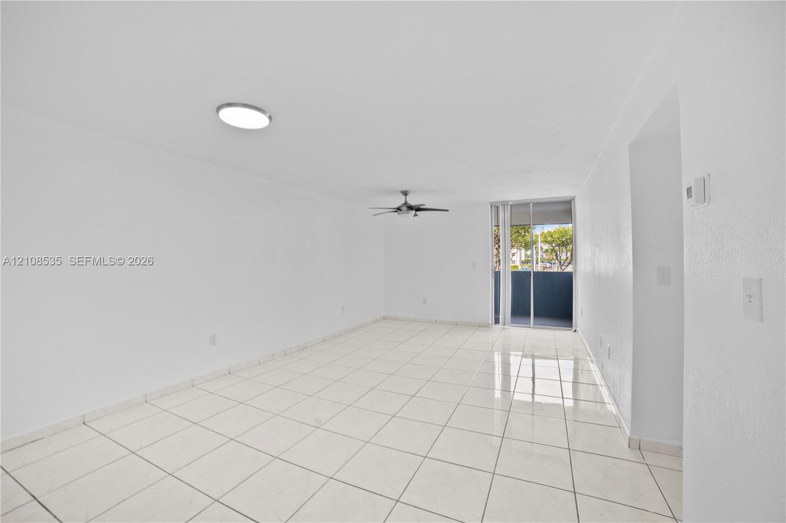 Neutral-toned tile flooring, ceiling-mounted flush lighting, multi-blade ceiling fan, and sliding glass doors with exterior access