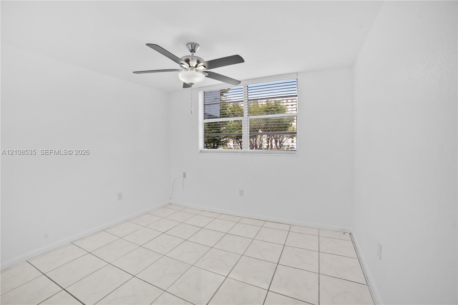 Neutral interior space featuring white tiled flooring, a multi-blade ceiling fan with integrated light fixture, and horizontal window blinds