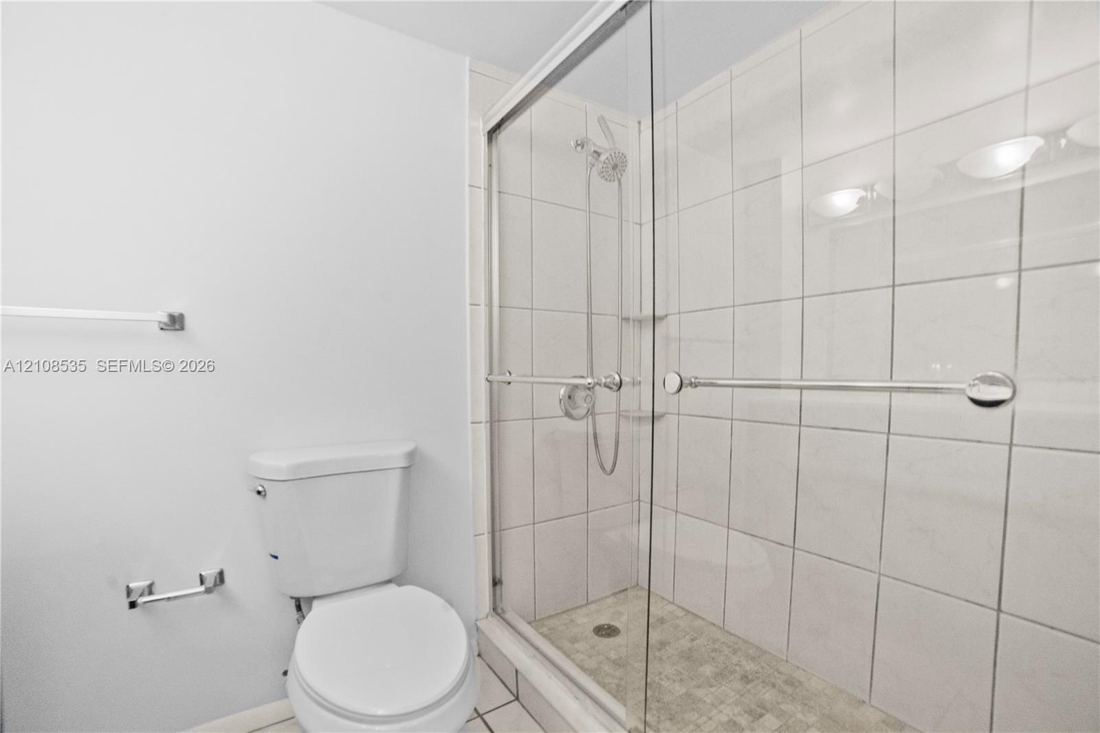 Walk-in shower with floor-to-ceiling tile surround, glass sliding door, integrated handheld shower fixture, and a stone-texture shower floor