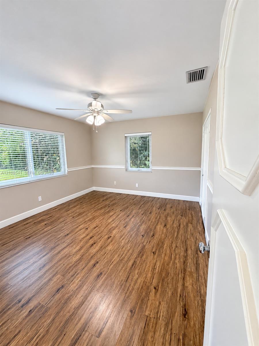 Wood-finish flooring, neutral wall tones, white chair rail molding, ceiling fan with integrated lighting, and multi-pane windows with horizontal blinds Wood-finish flooring, neutral wall tones, white chair rail molding, ceiling fan with integrated lighting, and multi-pane windows with horizontal blinds
