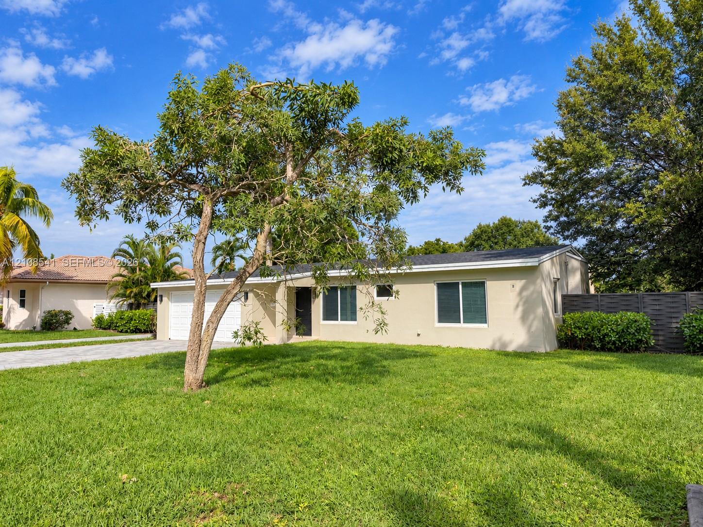 Single-story exterior featuring light-toned stucco siding, a two-car garage, mature landscaping, and an expansive lawn Single-story exterior featuring light-toned stucco siding, a two-car garage, mature landscaping, and an expansive lawn