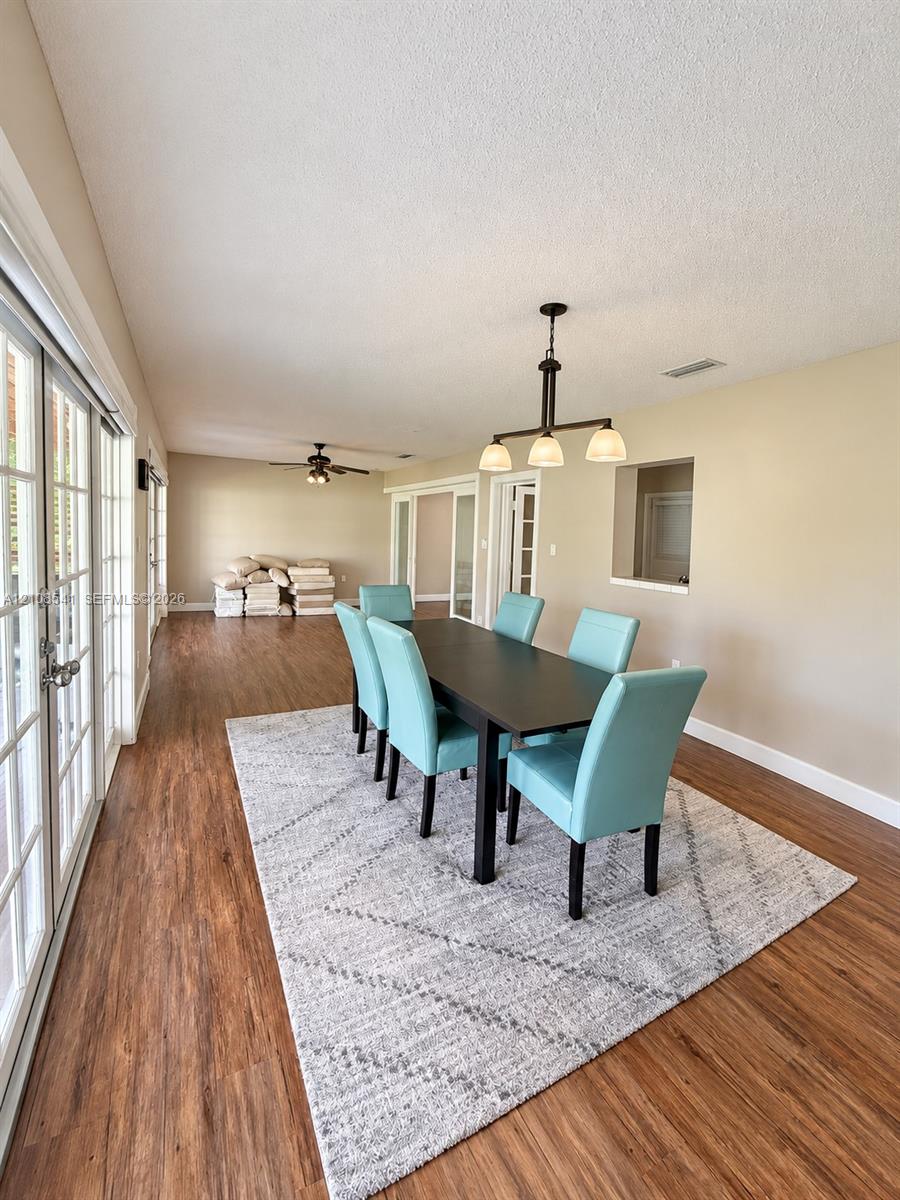Wood-finish flooring, multi-panel sliding glass doors, overhead ceiling fans, and a three-light linear pendant fixture Wood-finish flooring, multi-panel sliding glass doors, overhead ceiling fans, and a three-light linear pendant fixture