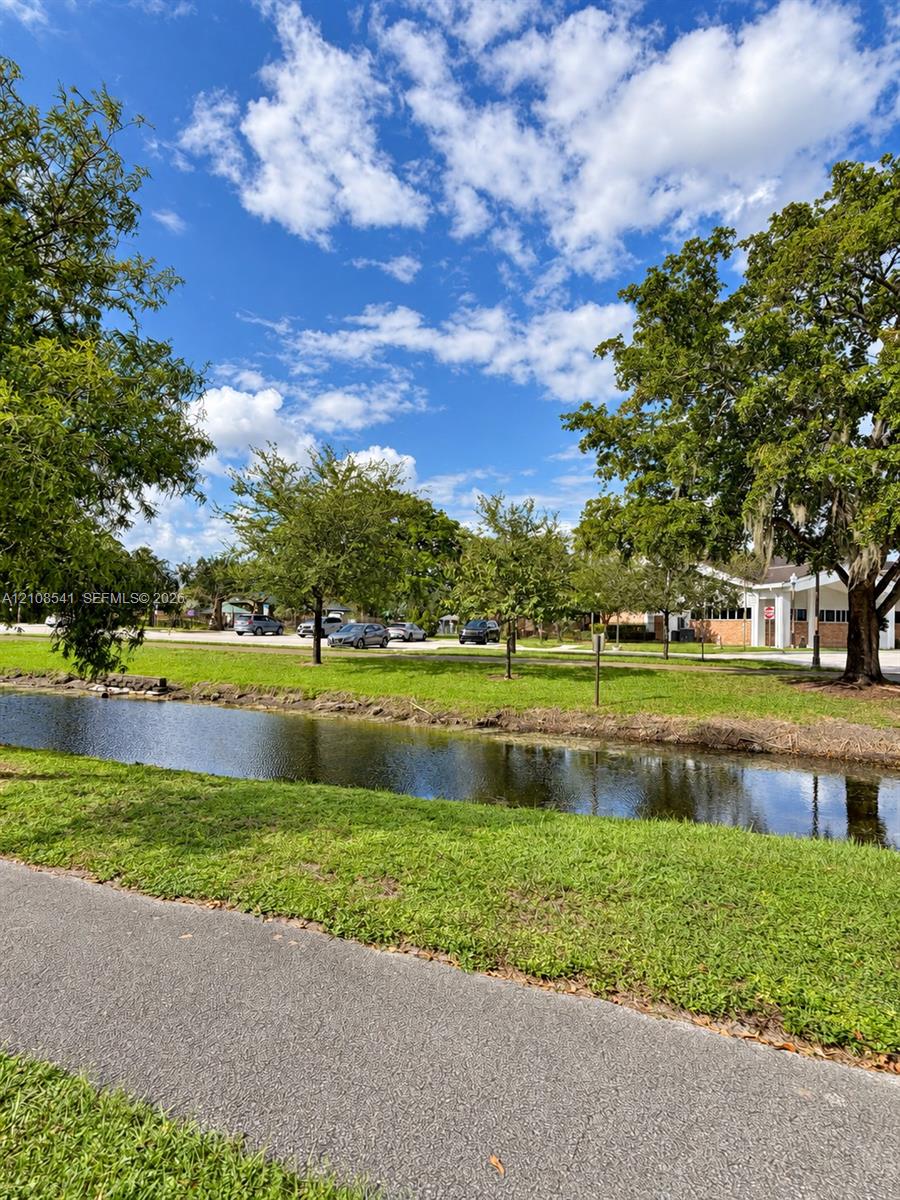 Waterfront exterior featuring a paved walking path, expansive green space, and mature trees
