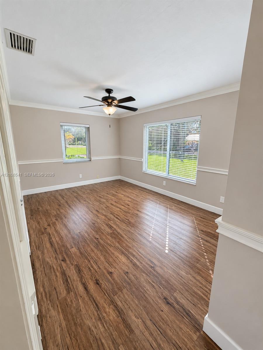 Room featuring wood-finish flooring, chair rail molding, crown molding, and a central ceiling fan with integrated lighting Room featuring wood-finish flooring, chair rail molding, crown molding, and a central ceiling fan with integrated lighting