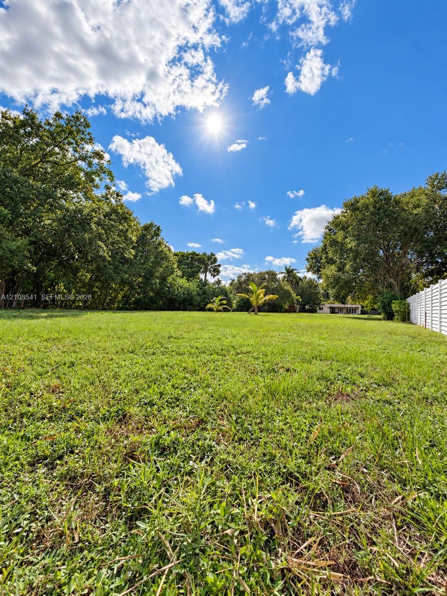 Expansive grounds featuring a grass lawn, mature trees, and a white privacy fence
