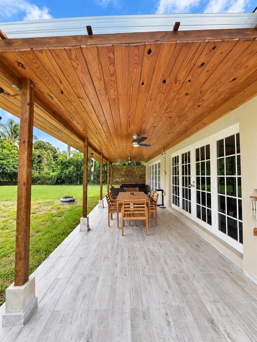 Covered patio featuring a wood-plank ceiling, wood-finish posts, light-toned plank flooring, and multi-panel glass french doors