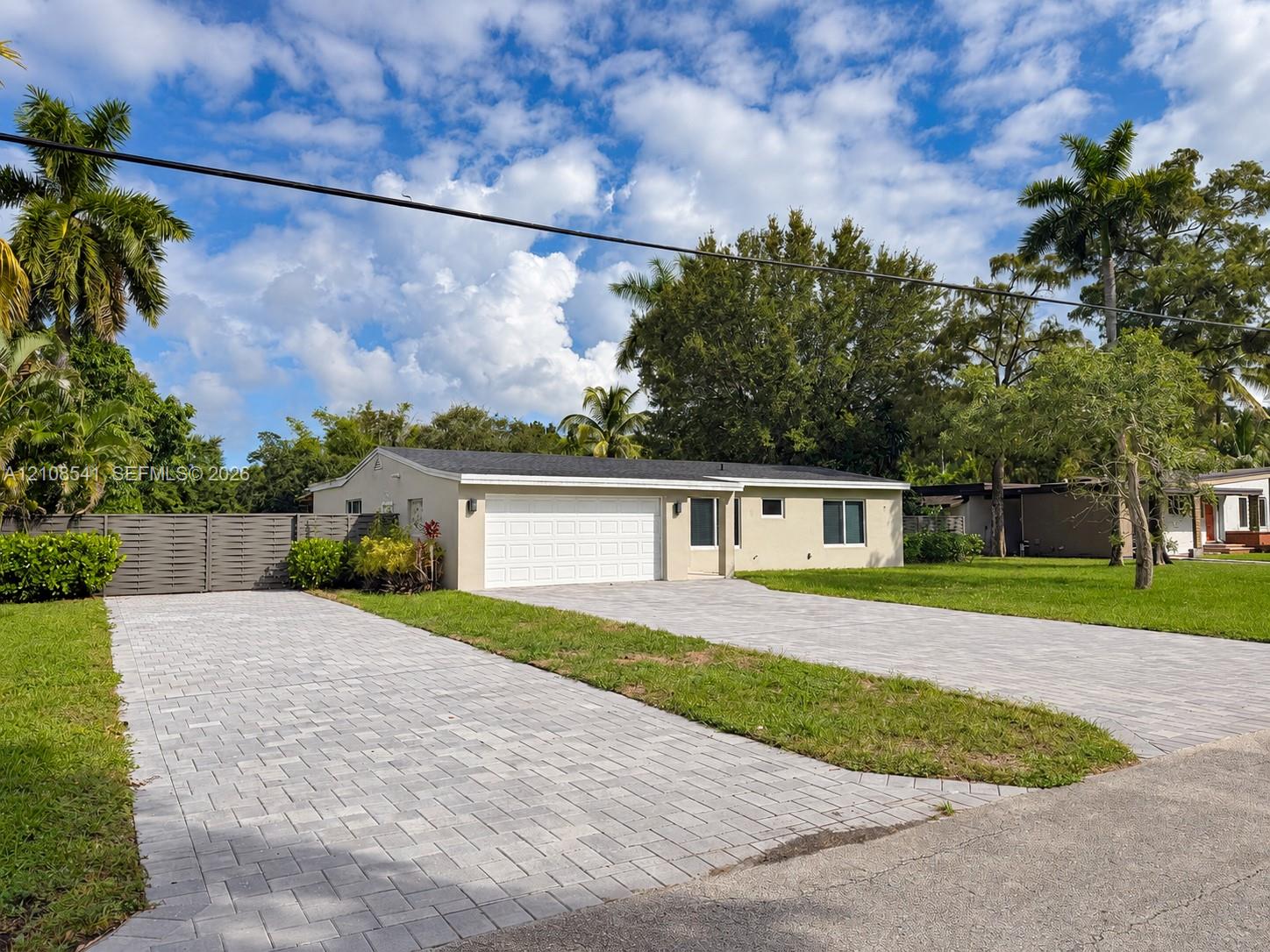 Single-story exterior featuring a paver driveway, an attached garage with a sectional door, and privacy fencing