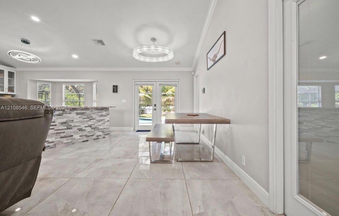 Large-format tile flooring, tiered tray ceiling, circular modern LED light fixtures, stone-veneer kitchen island, and French doors Large-format tile flooring, tiered tray ceiling, circular modern LED light fixtures, stone-veneer kitchen island, and French doors