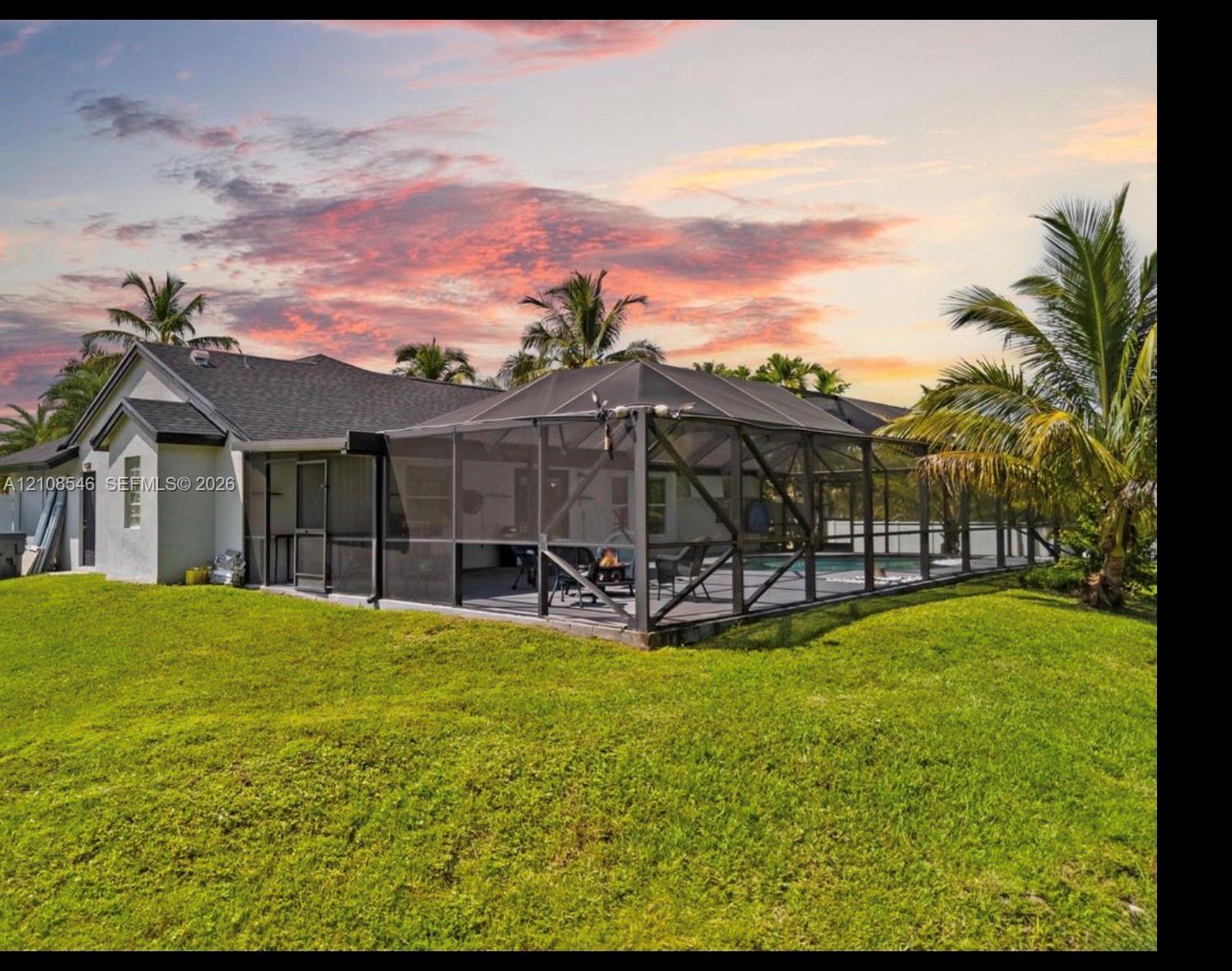 Exterior featuring a screened-in lanai, concrete-tiled roofing, manicured lawn, and mature palm trees