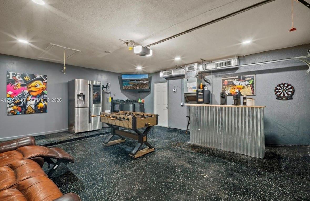 Garage space featuring an epoxy-coated floor, recessed lighting, and a built-in bar with a corrugated metal facade