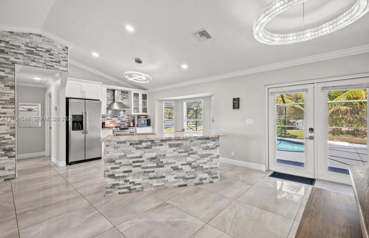 Kitchen featuring a stacked stone kitchen island, stainless steel refrigerator, tile flooring, recessed lighting, and double glass doors Kitchen featuring a stacked stone kitchen island, stainless steel refrigerator, tile flooring, recessed lighting, and double glass doors
