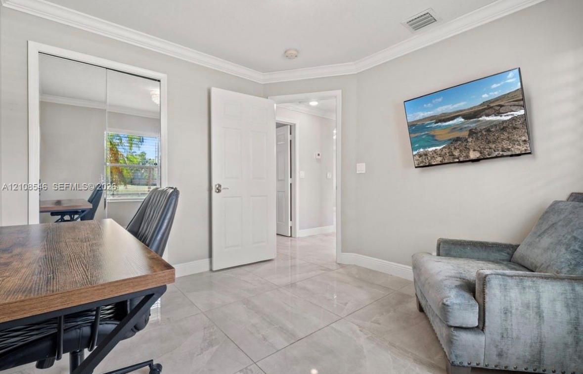 Neutral-toned room featuring large-format tile flooring, crown molding, a sliding mirrored closet door, and a six-panel interior door