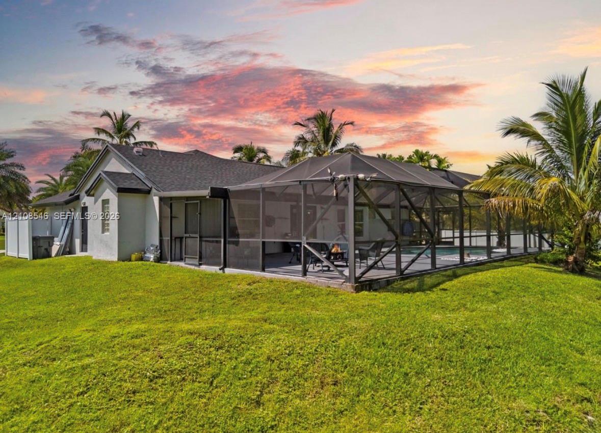 Exterior featuring a rear screened-in lanai with a swimming pool, expansive lawn, mature palm trees, and light-colored stucco siding