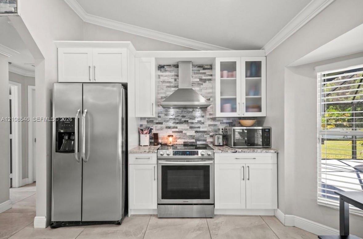 Kitchen featuring white cabinetry, stainless steel appliances, a stone-patterned backsplash, quartz countertops, and ceramic tile flooring