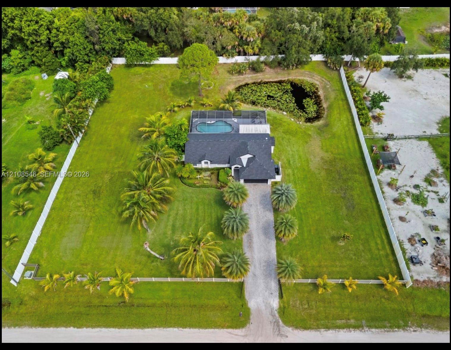Expansive lot featuring a fenced perimeter, a swimming pool with a screened enclosure, a private pond, and extensive palm tree landscaping Expansive lot featuring a fenced perimeter, a swimming pool with a screened enclosure, a private pond, and extensive palm tree landscaping