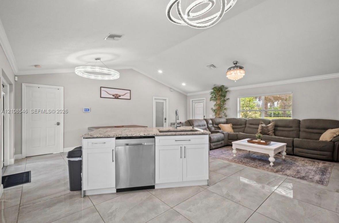 Open-concept living space featuring vaulted ceilings, oversized tile flooring, white cabinetry with stone countertops, stainless steel dishwasher, and contemporary circular chandelier lighting