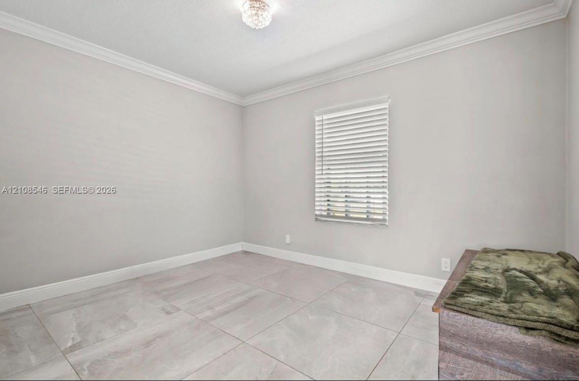Neutral-toned room featuring large-format stone-finish floor tiling, crown molding, and a single window with horizontal blinds