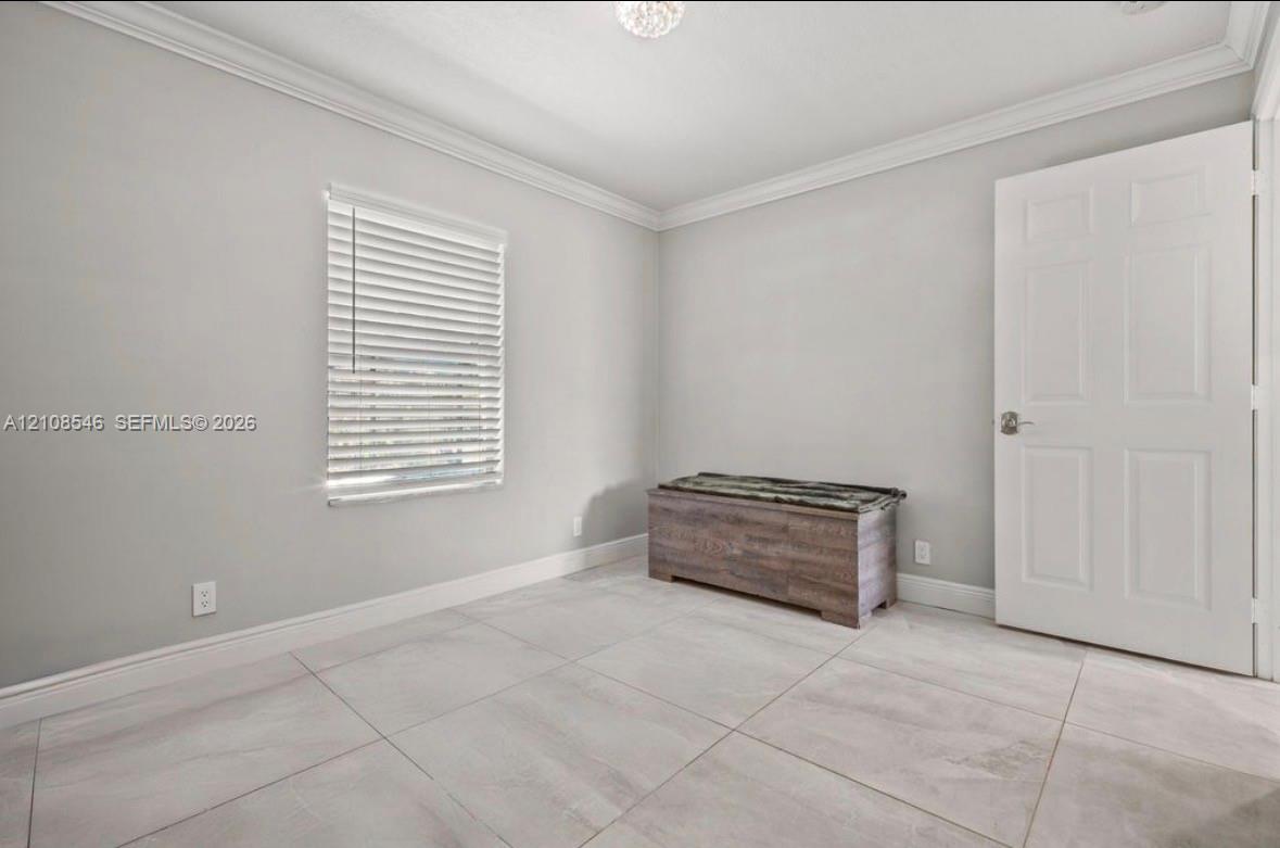 Neutral-toned interior space featuring large-format ceramic tile flooring, crown molding, a multi-panel interior door, and horizontal window blinds