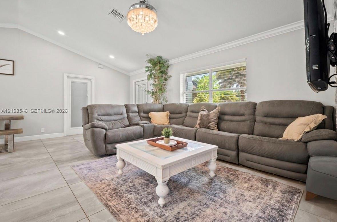 Living space featuring vaulted ceilings, oversized tile flooring, crown molding, recessed lighting, and a crystal chandelier