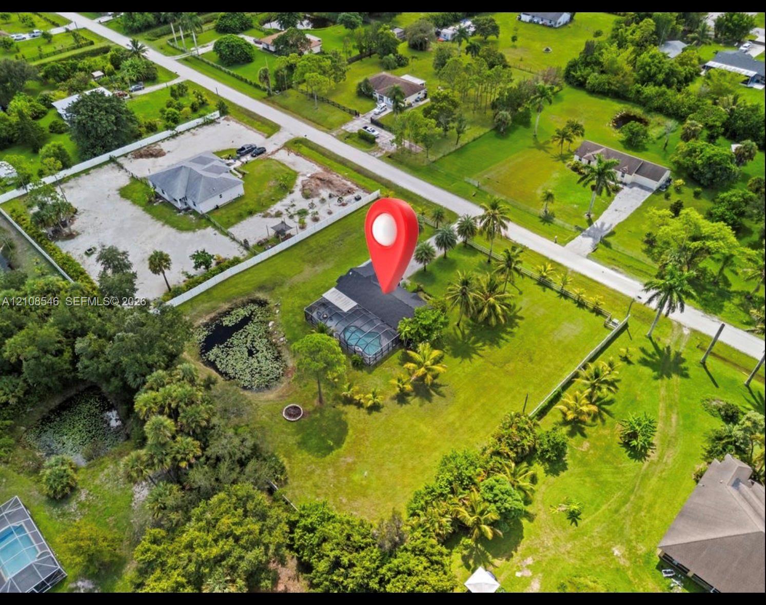 Aerial perspective of a property featuring an expansive grass lawn, mature palm trees, a screened-in pool enclosure, and a private pond