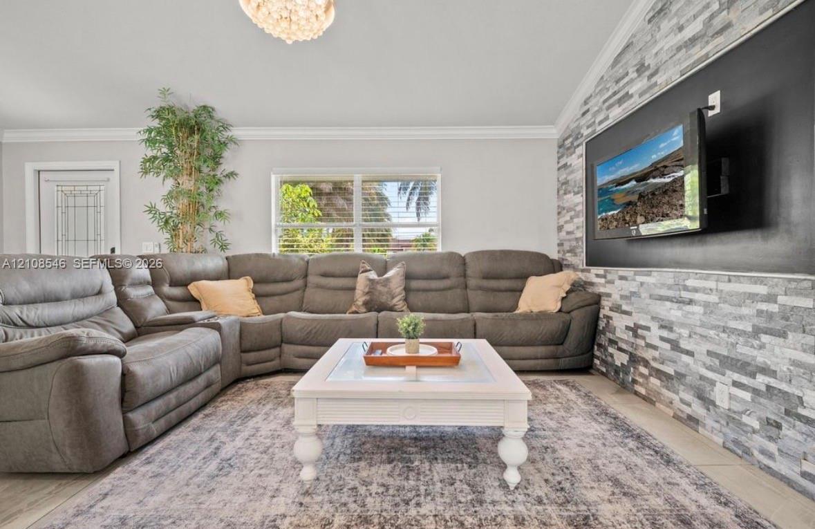 Vaulted ceiling featuring a decorative chandelier, stacked stone accent wall, and crown molding
