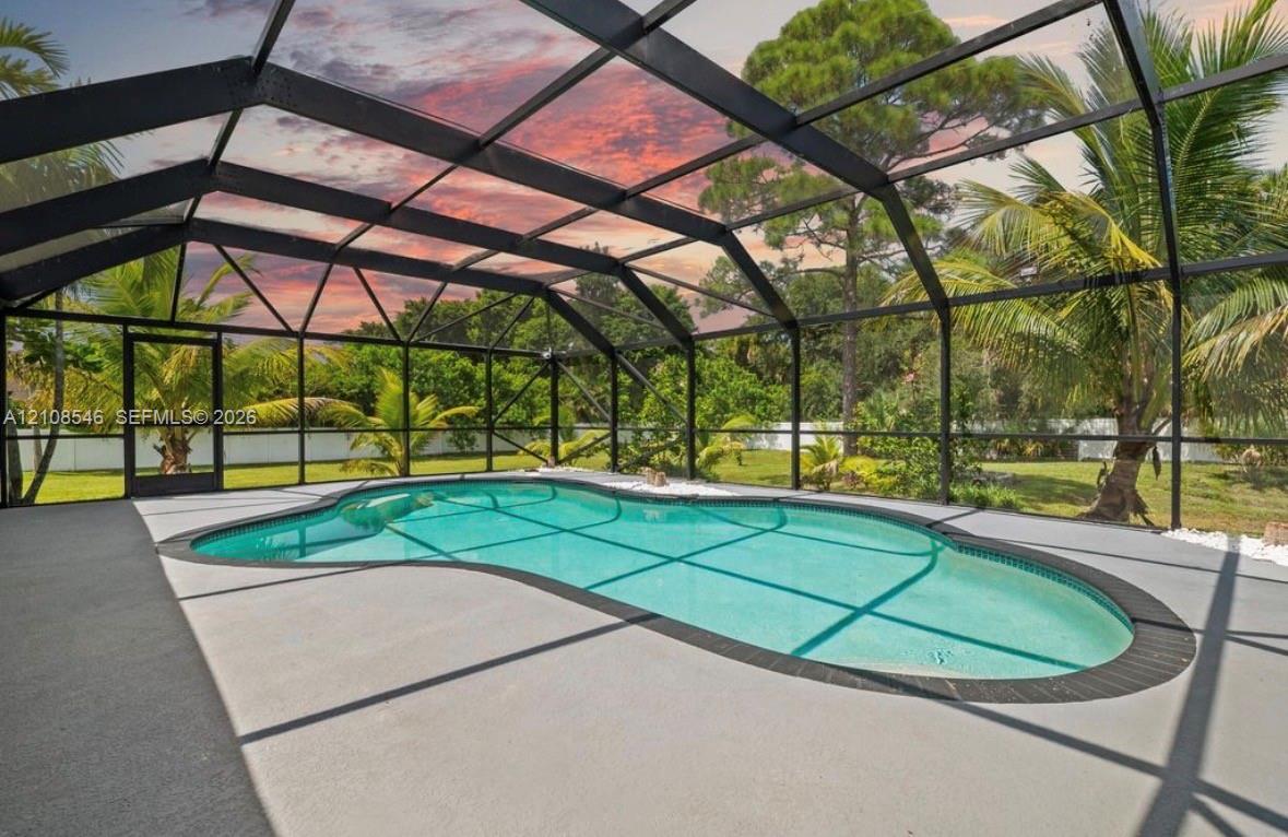Free-form swimming pool with a tile surround, encased in a screened-in aluminum lanai structure featuring a concrete deck and lush tropical landscaping Free-form swimming pool with a tile surround, encased in a screened-in aluminum lanai structure featuring a concrete deck and lush tropical landscaping