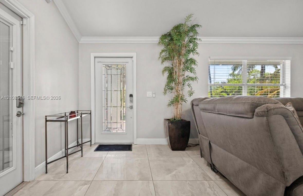Large-format tile flooring, vaulted ceilings with crown molding, and an entry door featuring decorative glass inlay