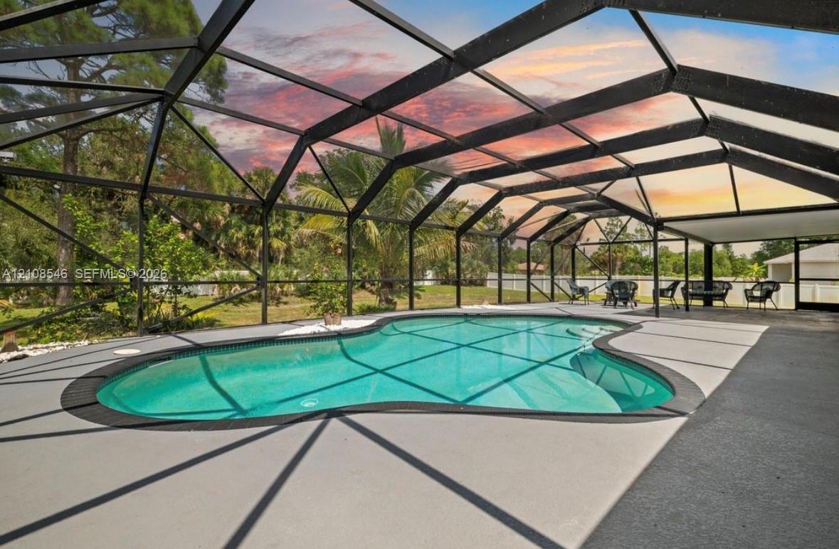 Screened-in patio featuring a freeform swimming pool, concrete deck, and perimeter fencing Screened-in patio featuring a freeform swimming pool, concrete deck, and perimeter fencing
