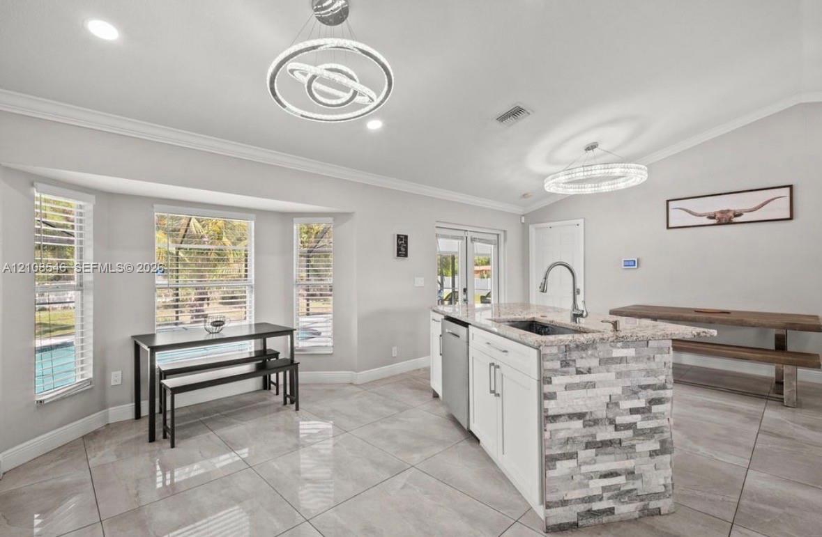 Kitchen featuring a stone-facade island with an integrated sink, polished stone countertops, custom white cabinetry, tile flooring, and contemporary orbital pendant lighting