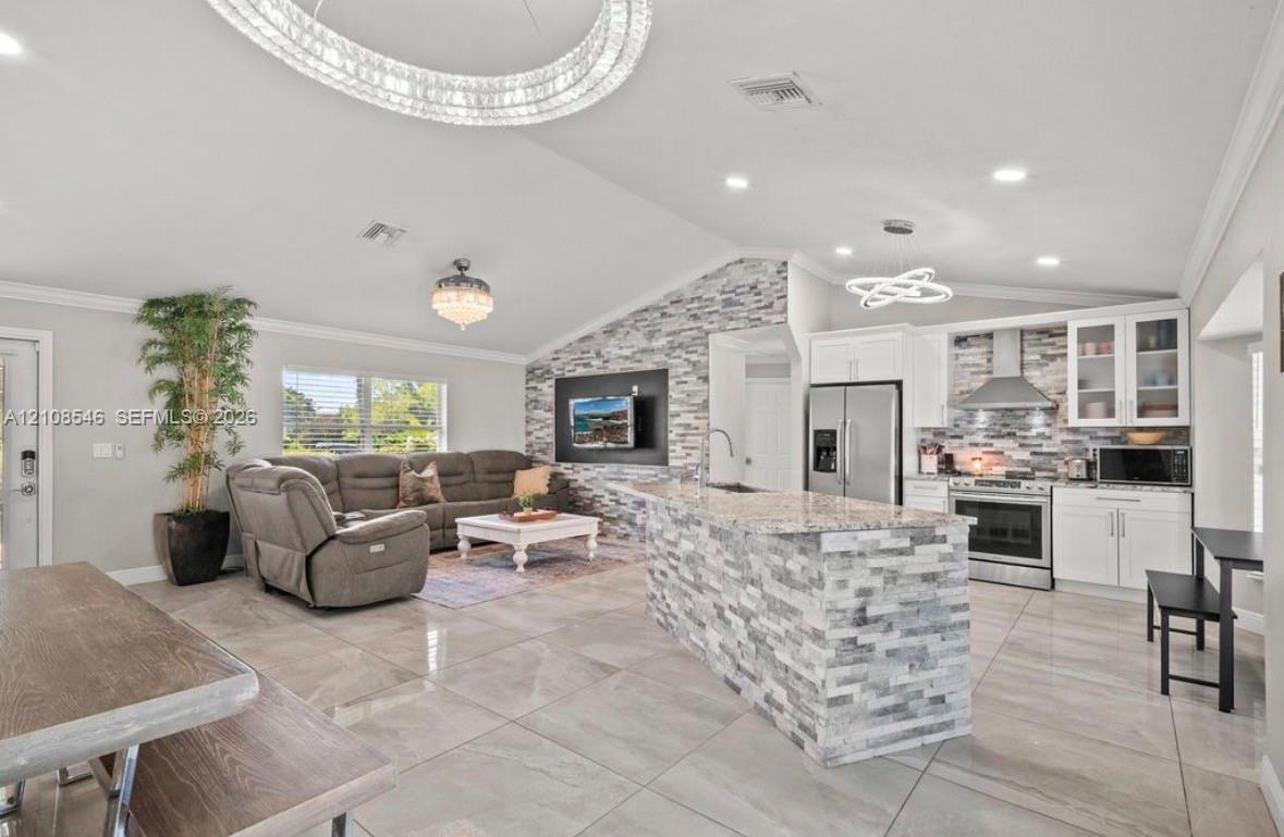 Open-concept area featuring stone-clad kitchen island, stacked stone accent wall, recessed lighting, modern geometric chandeliers, and large-format tile flooring Open-concept area featuring stone-clad kitchen island, stacked stone accent wall, recessed lighting, modern geometric chandeliers, and large-format tile flooring