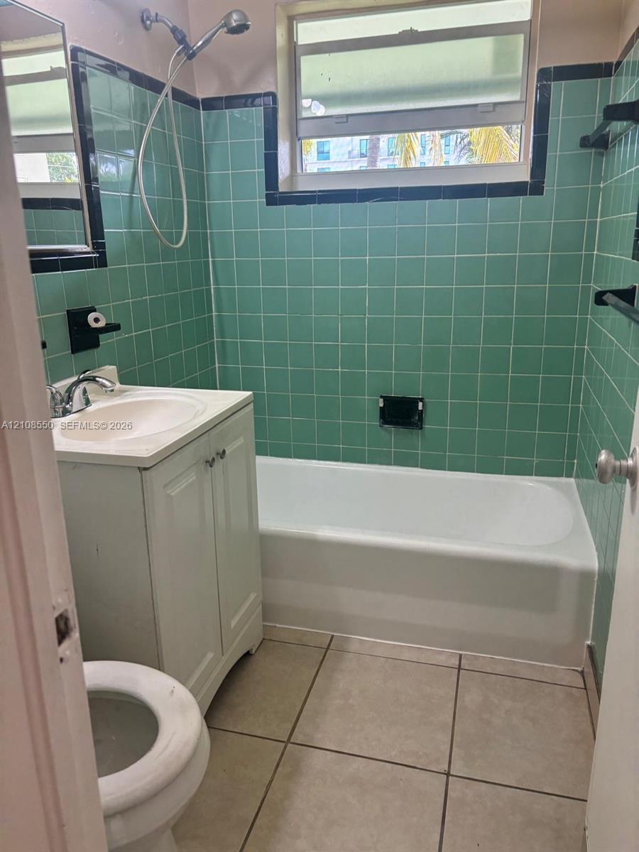 Bathroom featuring full-height ceramic tile walls with accent trim, built-in tub and shower combination, white vanity cabinet with a integrated basin, and neutral floor tile