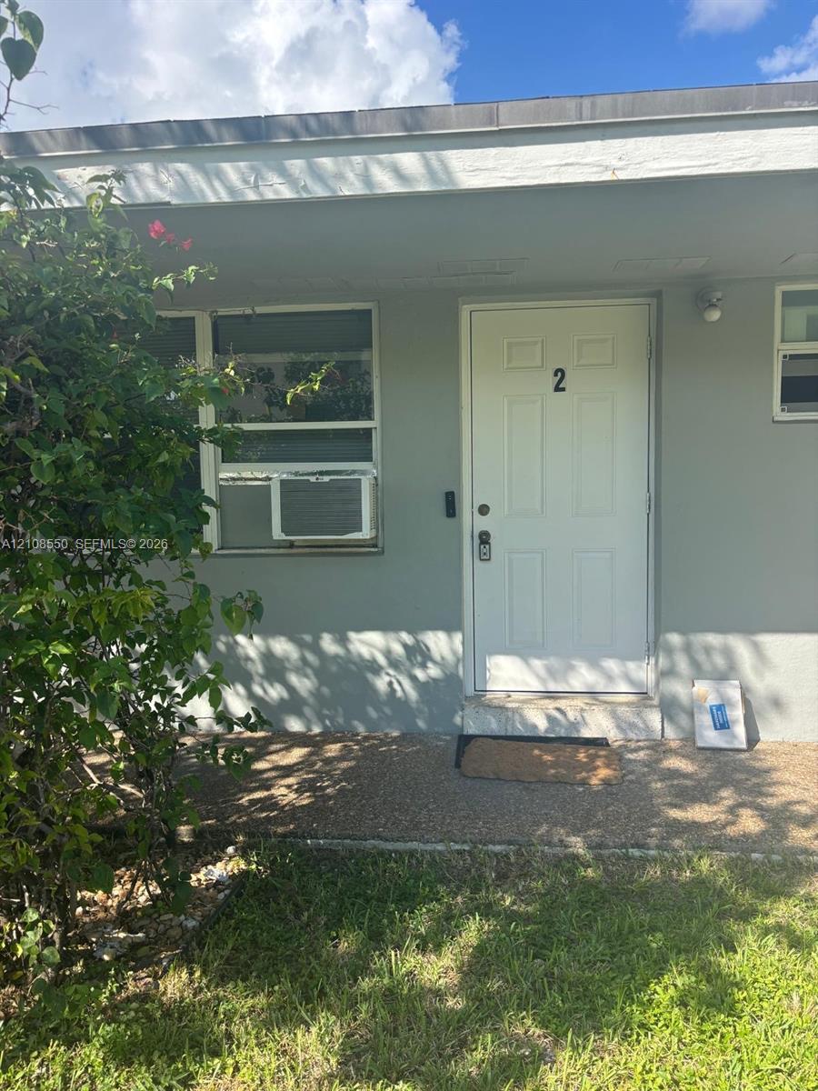 Exterior entry featuring a painted masonry facade, a paneled door, horizontal sliding window, and a covered concrete stoop