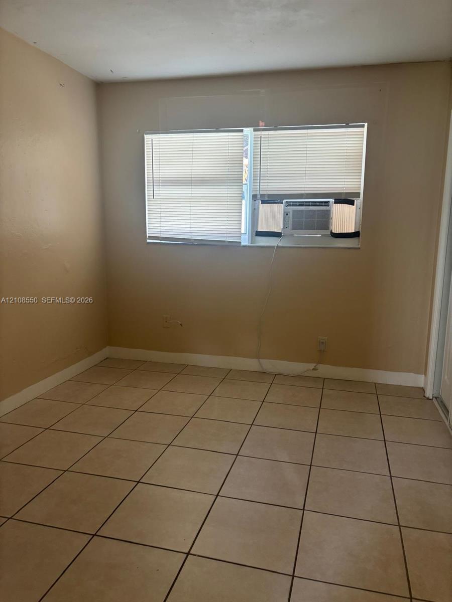 Neutral-toned interior space featuring light-colored ceramic tile flooring, a dual-pane horizontal window with integrated blinds, and painted walls