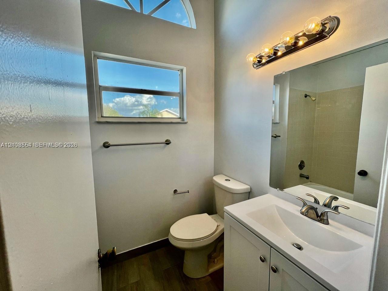 Bathroom featuring a single-sink vanity with a solid-surface countertop, wood-finish flooring, an arched transom window, and a multi-light wall-mounted fixture