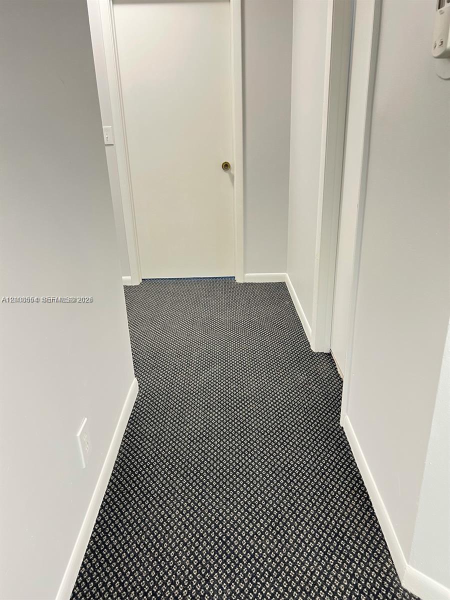 Hallway featuring neutral wall paint, geometric patterned carpeting, and a solid-core interior door with a brushed metal handle