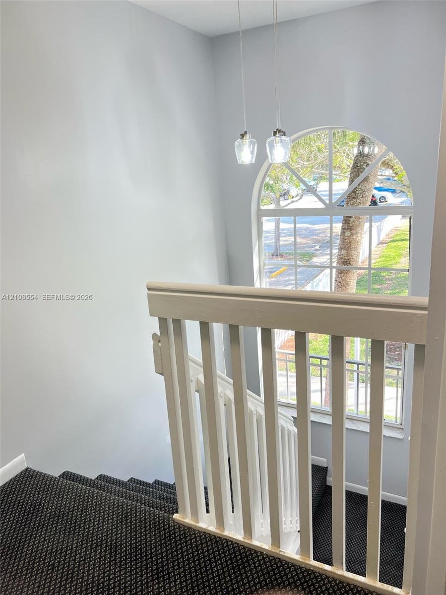 Stairwell featuring white wooden balusters, an arched window with muntin detailing, and dual pendant light fixtures
