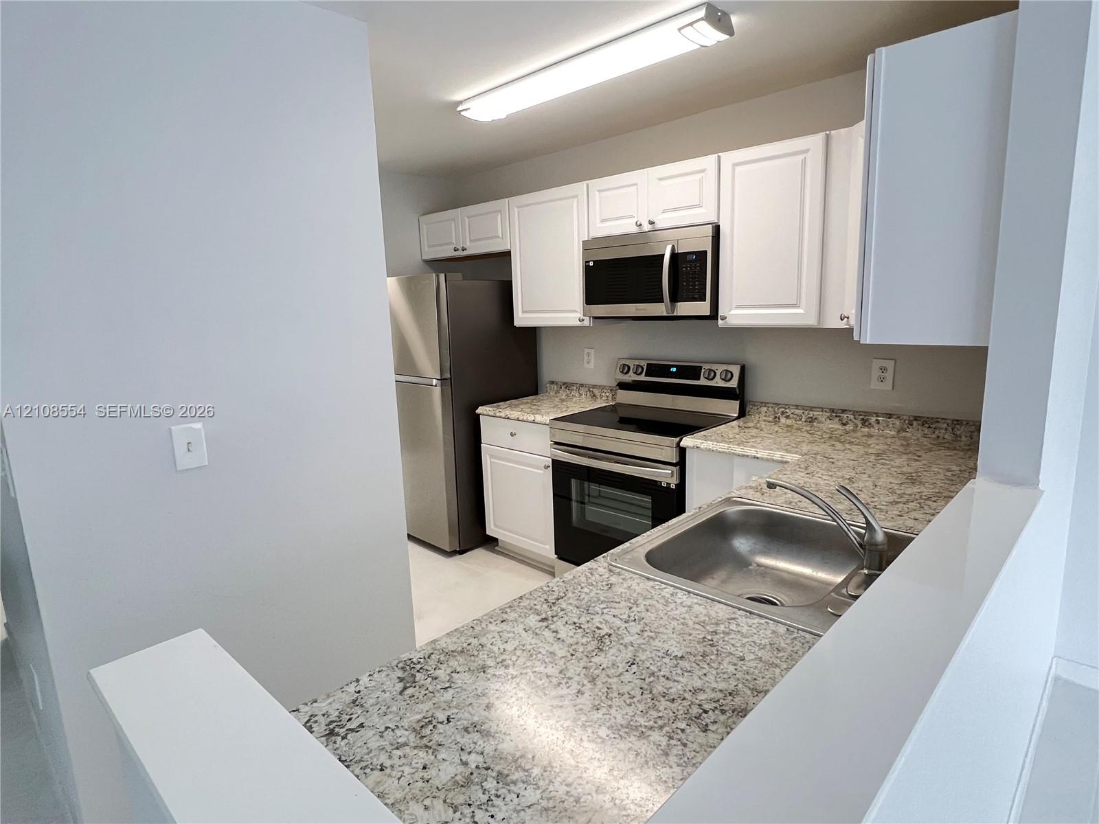 Kitchen featuring white shaker-style cabinetry, stone-finish countertops, stainless steel appliances, and a single-basin undermount sink with a gooseneck faucet