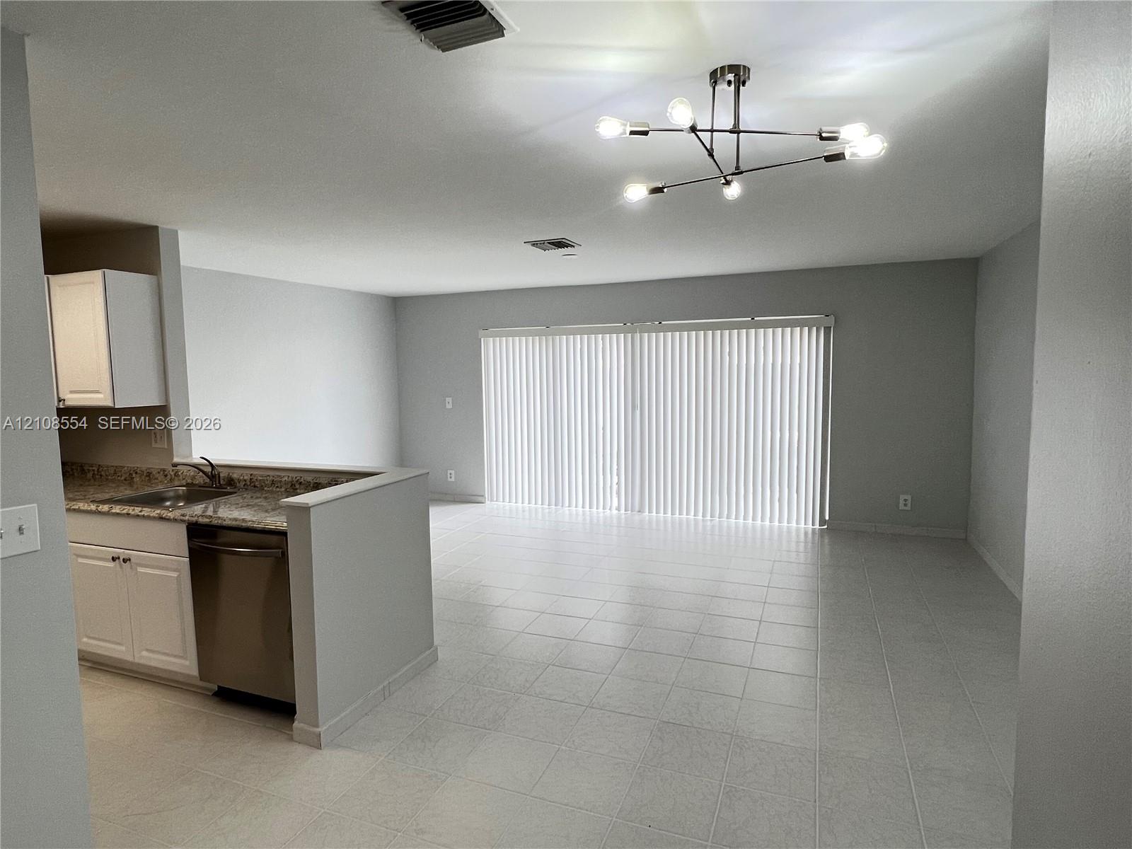 Kitchen featuring white cabinetry, stone-surface countertops, and a stainless steel dishwasher, accented by tile flooring and a multi-arm geometric light fixture