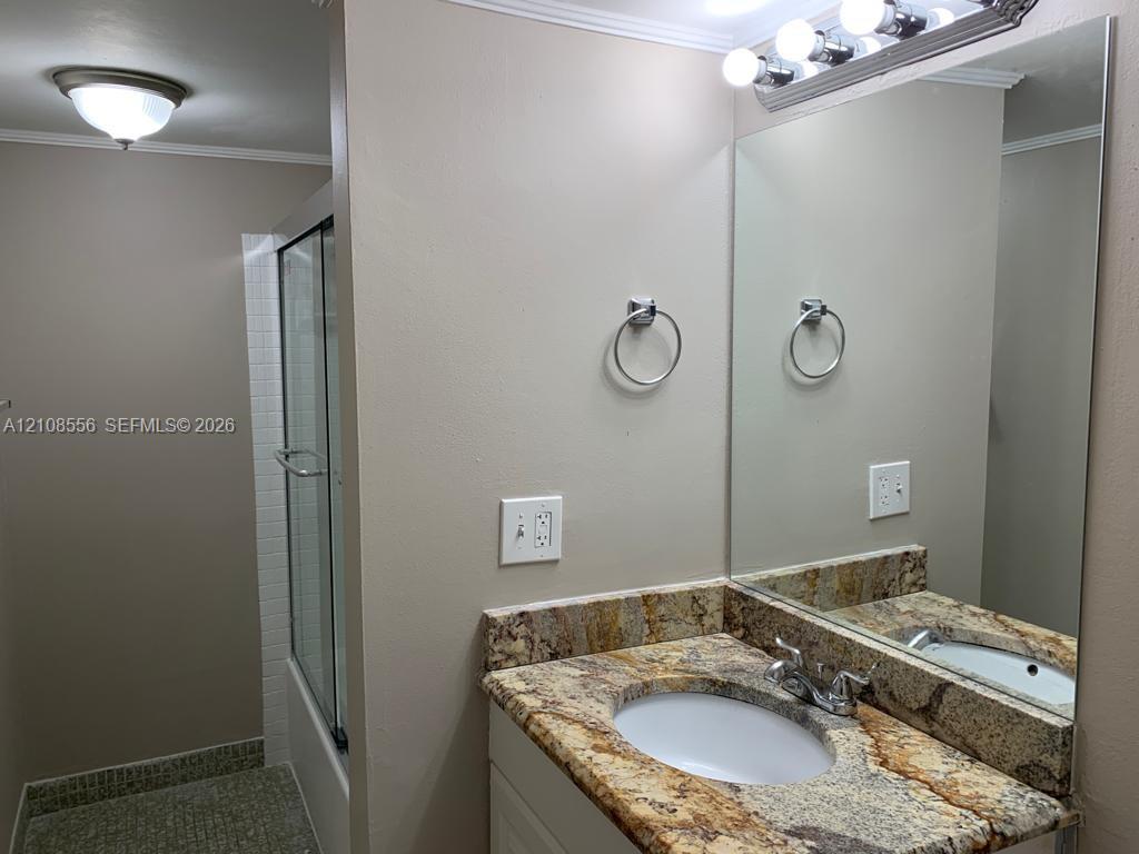 Vanity featuring stone countertop with integrated sink, full-width wall mirror, four-light vanity fixture, and enclosed glass shower