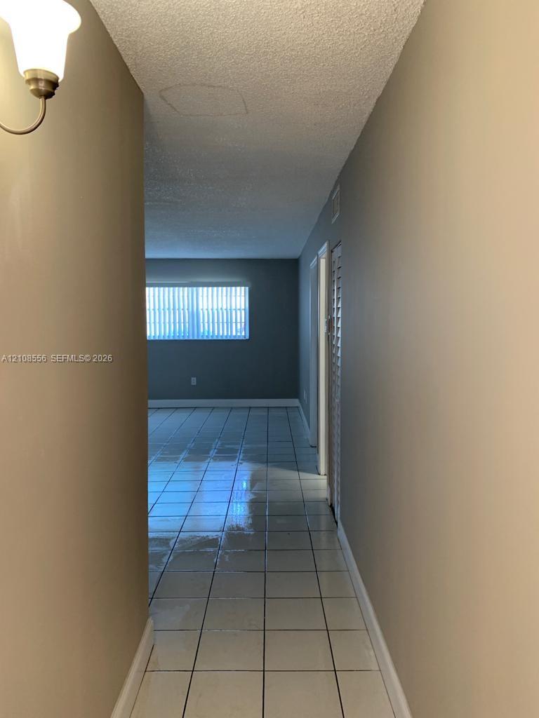Hallway featuring tile flooring, neutral wall paint, a wall-mounted light fixture, and louvered closet doors Hallway featuring tile flooring, neutral wall paint, a wall-mounted light fixture, and louvered closet doors