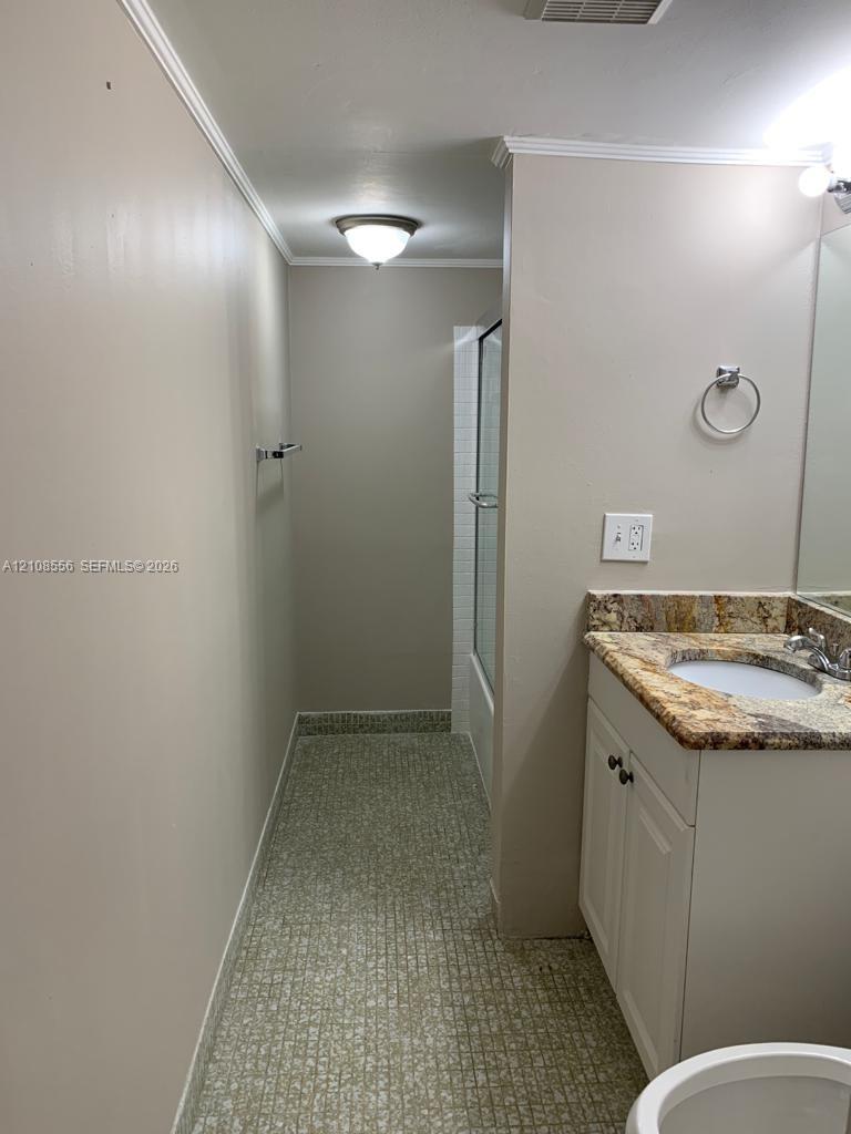 Bathroom featuring a stone-look countertop, integrated vanity cabinet, flush-mount ceiling lighting, and a shower enclosure with a glass door