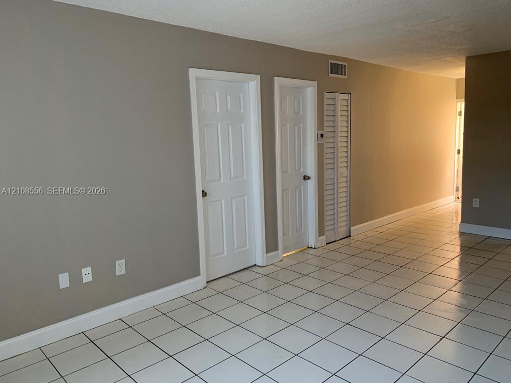 Neutral-toned interior featuring white ceramic floor tile, two interior paneled doors, and a louvered closet door Neutral-toned interior featuring white ceramic floor tile, two interior paneled doors, and a louvered closet door
