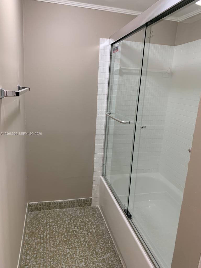 Tub and shower combination featuring a glass sliding enclosure, white tiled surround, chrome fixtures, and patterned flooring
